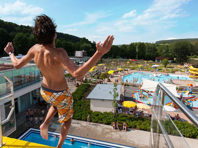 Mann auf Sprungturm mit Blick auf das Freibad