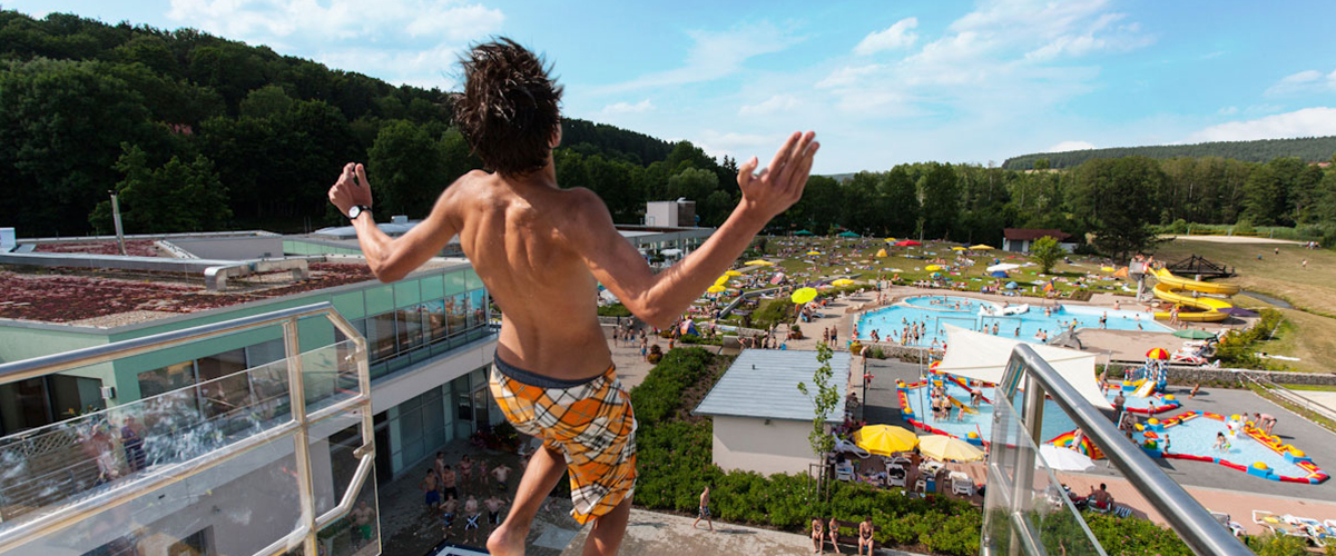 Mann auf Sprungturm mit Blick auf das Freibad