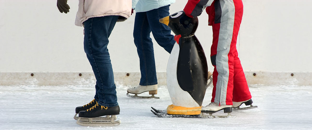 drei Personen mit Laufhilfe auf der Eislaufbahn