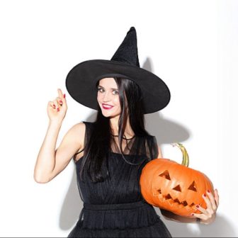 Young woman in hat and dress as a witch on white background