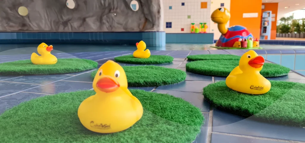 Kleine gelbe Badeenten auf grünen Kunstrasenkreisen im Kinderbereich