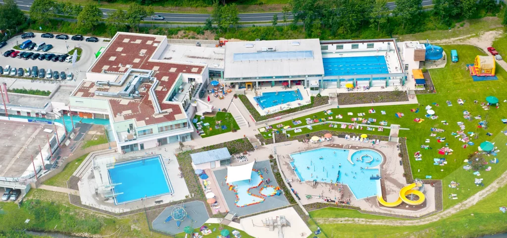 Luftaufnahme des gesamten Schwimmbades mit Gebäuden, Becken und Liegewiese