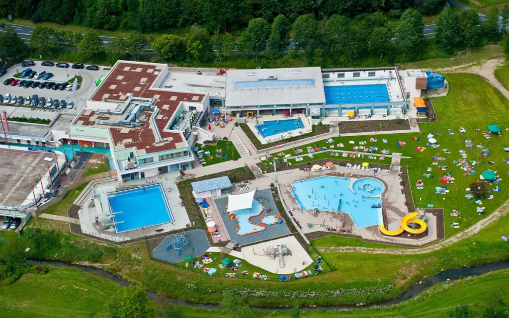 Luftaufnahme des gesamten Schwimmbades mit Gebäuden, Becken und Liegewiese