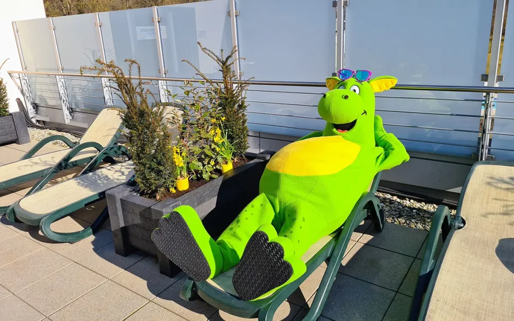 Maskottchen Cabriolino der grüne Drache sonnt sich auf einer Außenliege